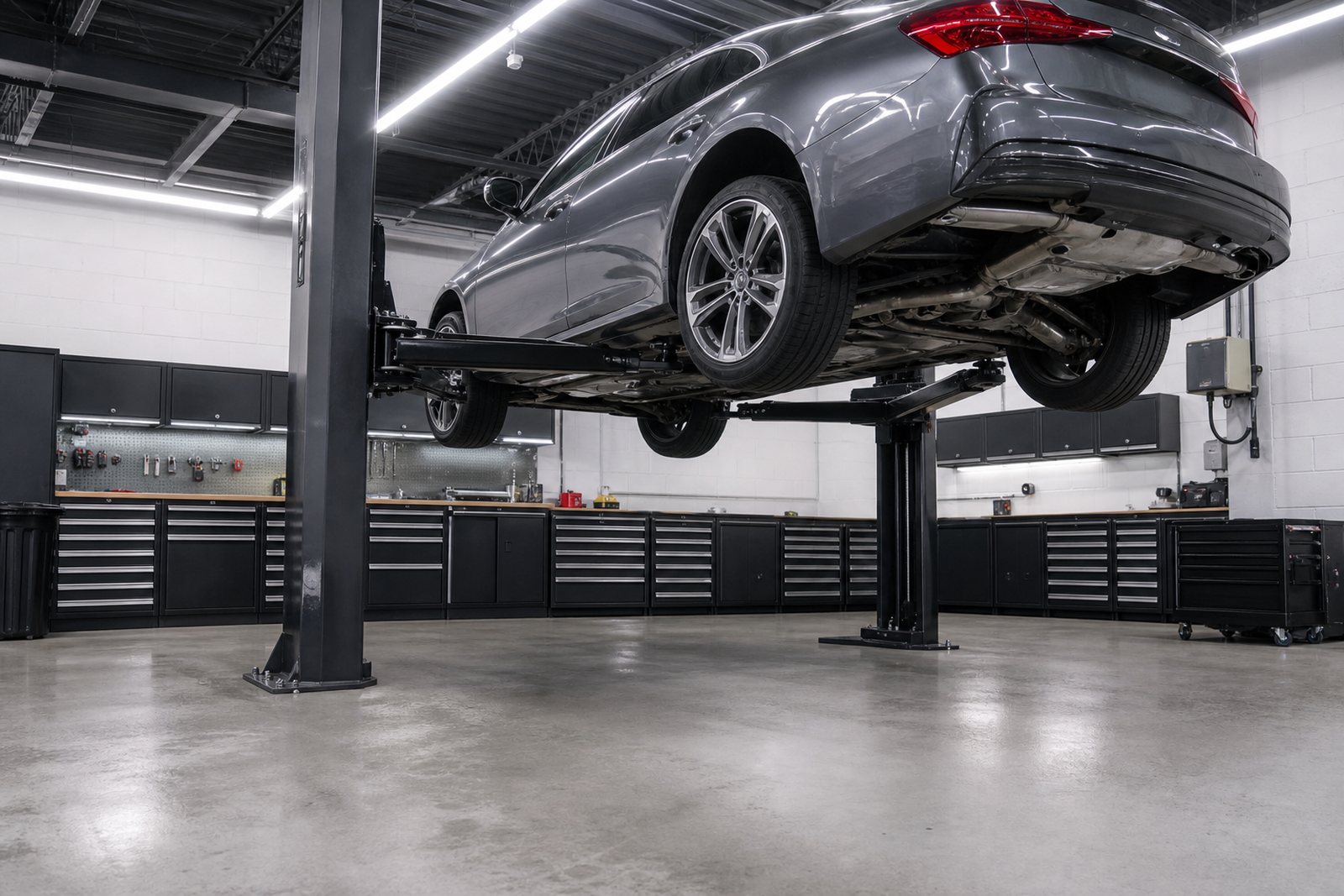 Car raised on a hydraulic lift in a tidy independent auto repair shop with tool chests along the wall